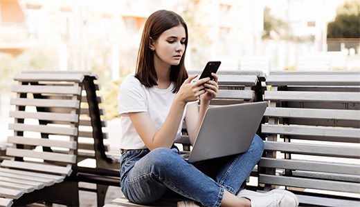 Woman on bench working on her smartphone and notebook.