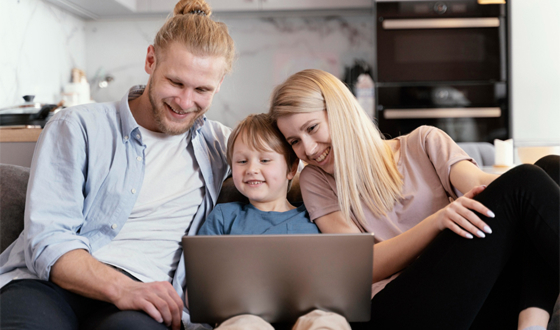 A smiling family of three sitting on a couch and looking at a laptop together.