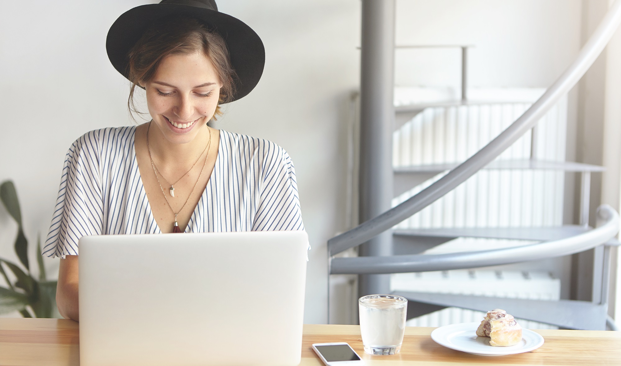 Fröhliche Frau, die an ihrem Küchentisch am Laptop arbeitet.